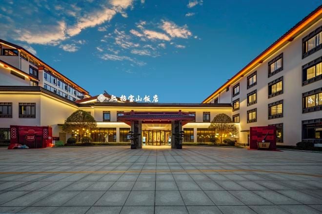 Entrada de hotel con arquitectura tradicional, un patio adoquinado y cielo despejado.