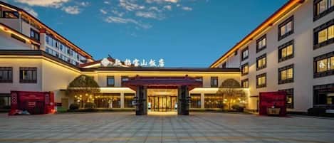 Entrada de hotel con arquitectura tradicional, un patio adoquinado y cielo despejado.