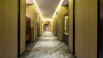 Een hotelgang met een lange, smalle indeling, houten lambrisering en een betegelde vloer.