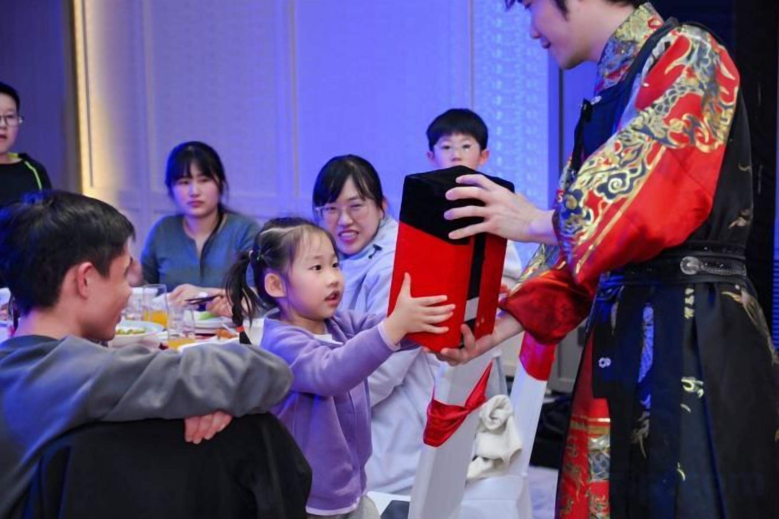 A group of people at a table with a person in traditional attire holding a red book.