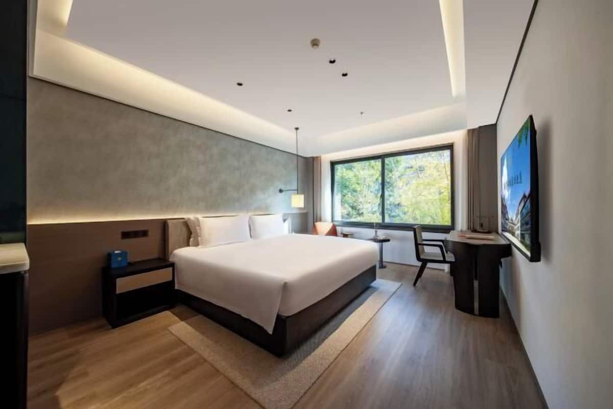 A modern bedroom with a large bed, a desk, and a window with a view of trees.