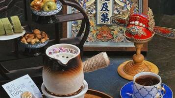 Um conjunto de chá tradicional com chaleira, xícaras e pires, uma tigela de nozes e um prato decorativo com frutas.