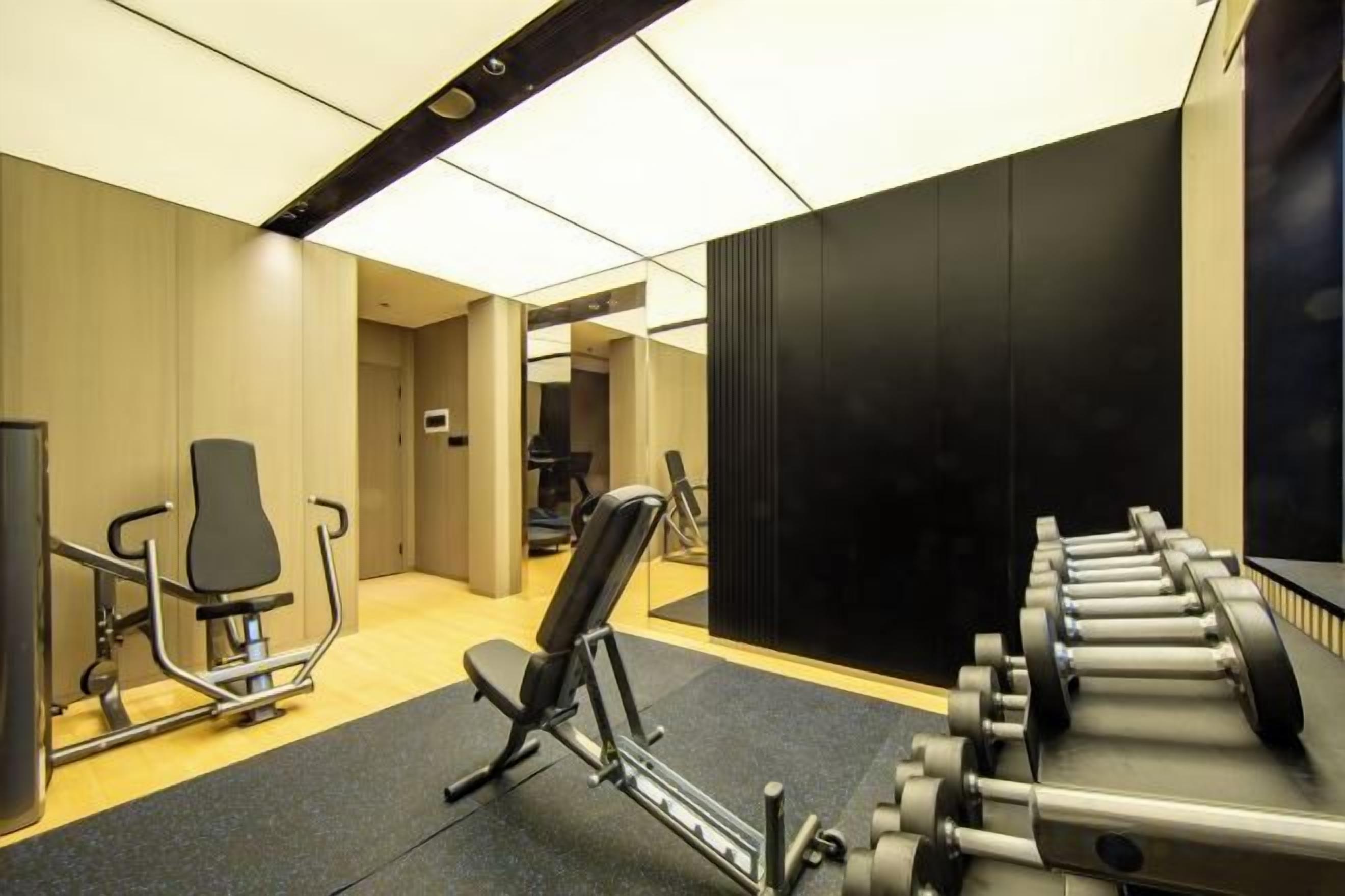 Ein Fitnessraum mit Trainingsgeräten, einem Spiegel und einer Tür zu einem weiteren Raum.