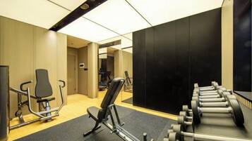 Ein Fitnessraum mit Trainingsgeräten, einem Spiegel und einer Tür zu einem weiteren Raum.