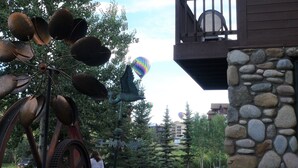 A rustic building with a stone wall and a balcony overlooking a street with trees and hot air balloons in the background. -  Ski History Unit with 2 decks, sleeps 2- walk to Base area for concerts (Mt Crested Butte)