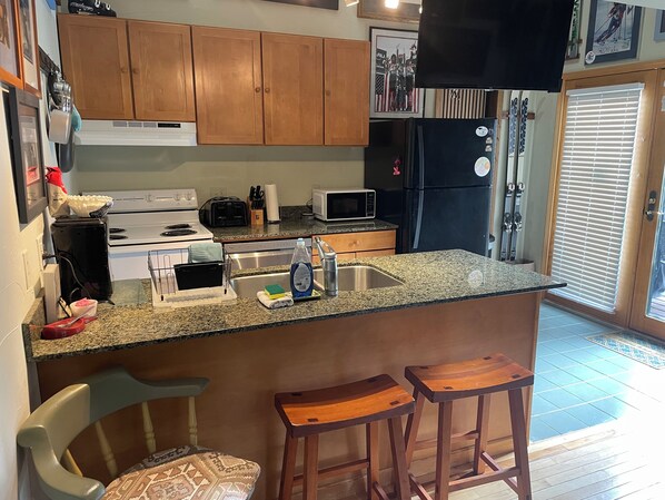 A kitchen with wooden cabinets, a microwave, a refrigerator, a sink, and two stools. - Ski History Unit with 2 decks, sleeps 2- walk to Base area for concerts (Mt Crested Butte)