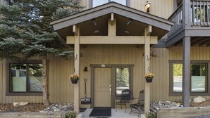 A wooden building with a covered entrance, a door labeled "1A", and two outdoor seating areas with metal chairs and potted plants. - French Street Haven | 5 Minute Walk to Main Street (Breckenridge)