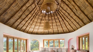 Um quarto com telhado de palha, janelas amplas, uma mesa de madeira e um sofá.