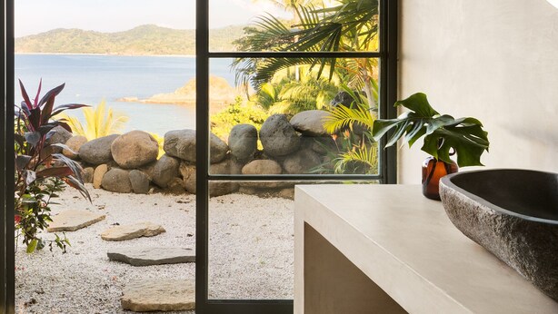 Um interior moderno com uma janela ampla que oferece vista para uma praia e palmeiras.