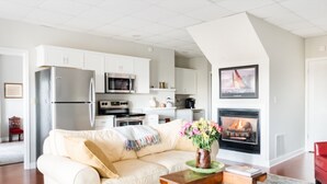 Een moderne woonkamer met een beige bank, een open haard en een keuken op de achtergrond.