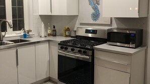 A modern kitchen with white cabinets, a stainless steel stove, a microwave, and a decorative seahorse painting on the wall.