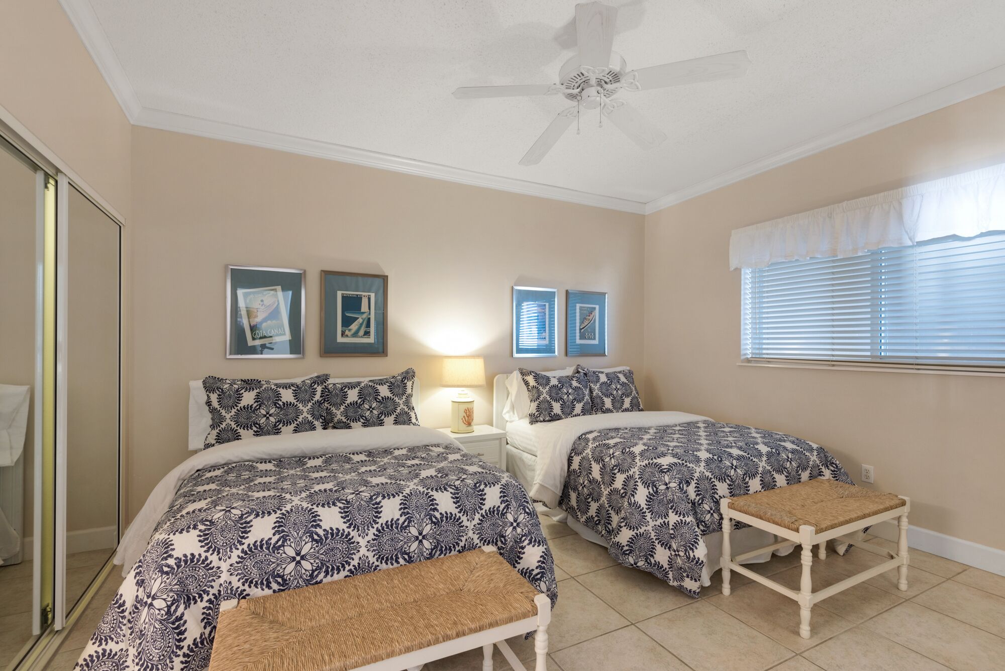 A bedroom with two beds, a ceiling fan, and framed pictures on the wall.