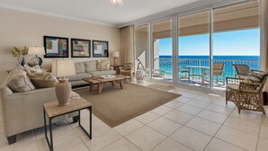 Uma sala de estar ampla com uma grande porta de vidro deslizante que dá para uma varanda com vista para o oceano.
