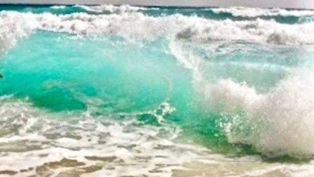 Uma praia com águas azul-turquesa e ondas brancas.
