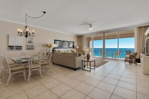 Relax in a spacious living area with a comfortable sofa set and dining table, surrounded by artwork and a sliding glass door leading to an ocean-view balcony.