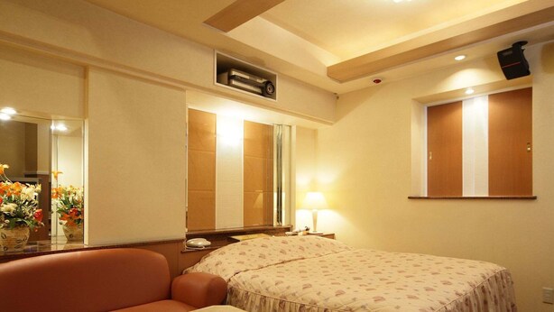 A hotel room with a bed, a small table, a sofa, a mirror, and a window with blinds. - Fine Sakai (Sakai)