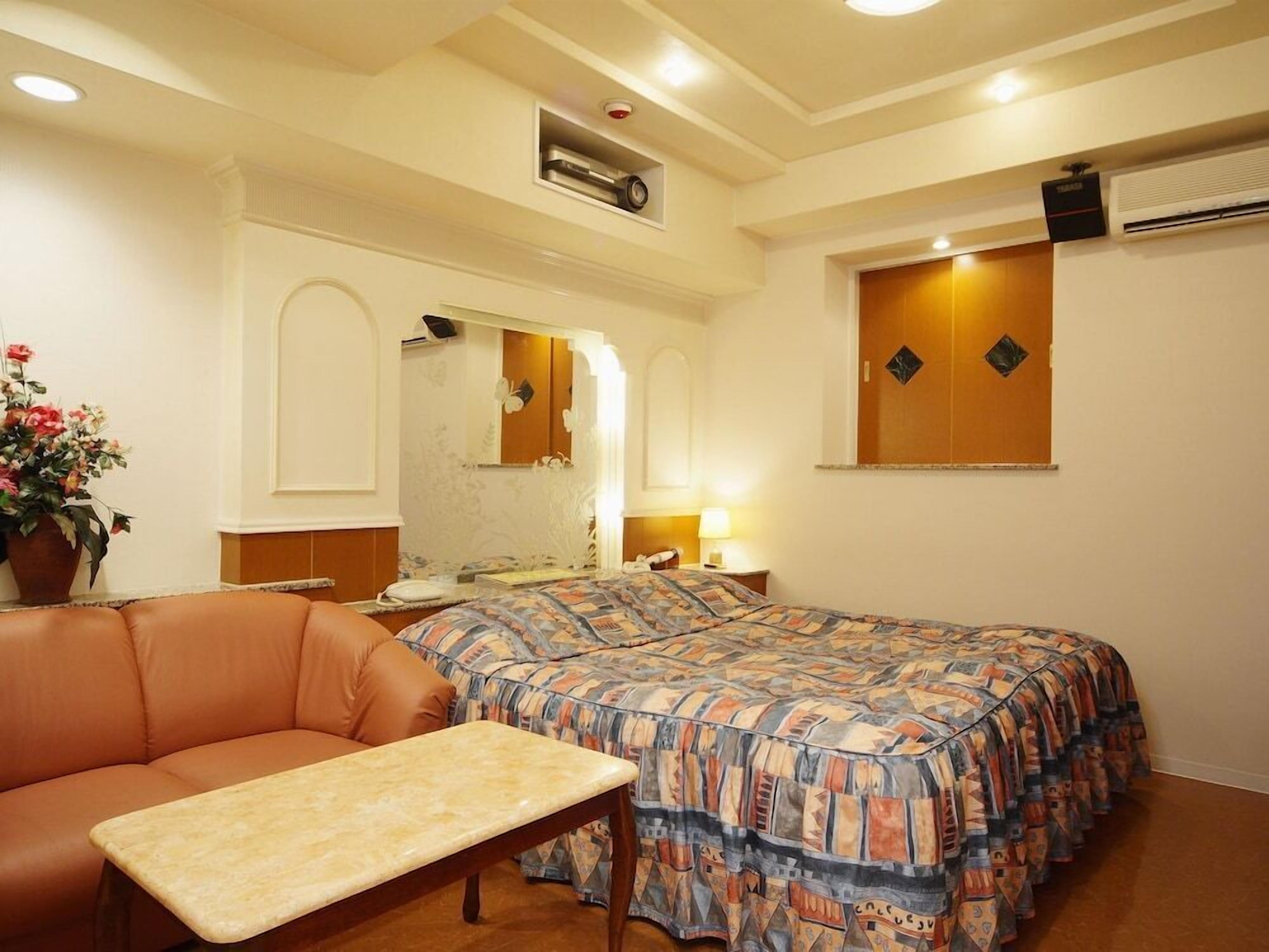Quarto de hotel com cama, sofá, mesa pequena, espelho e ar condicionado.