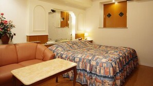 A hotel room with a bed, a sofa, a small table, a mirror, and an air conditioning unit. - Fine Sakai (Sakai)