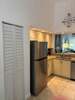 A kitchen with a stainless steel refrigerator, white cabinets, a granite countertop, and a window with a view.