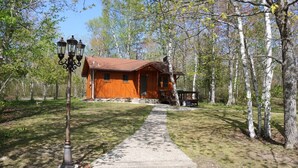 A wooden cabin with a red roof, surrounded by trees and a concrete path leading to it. - Private log cabin with view overlooking Grand Lake (Presque Isle)