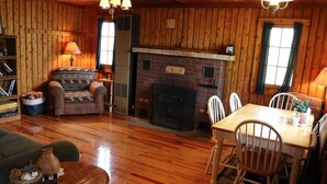 A cozy cabin interior with a fireplace, wooden walls, a dining area, and a comfortable seating arrangement. - Private log cabin with view overlooking Grand Lake (Presque Isle)