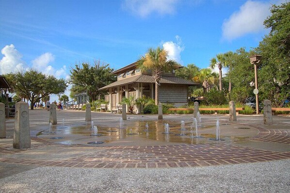 A courtyard with a fountain, a building with a tiled roof, and palm trees.