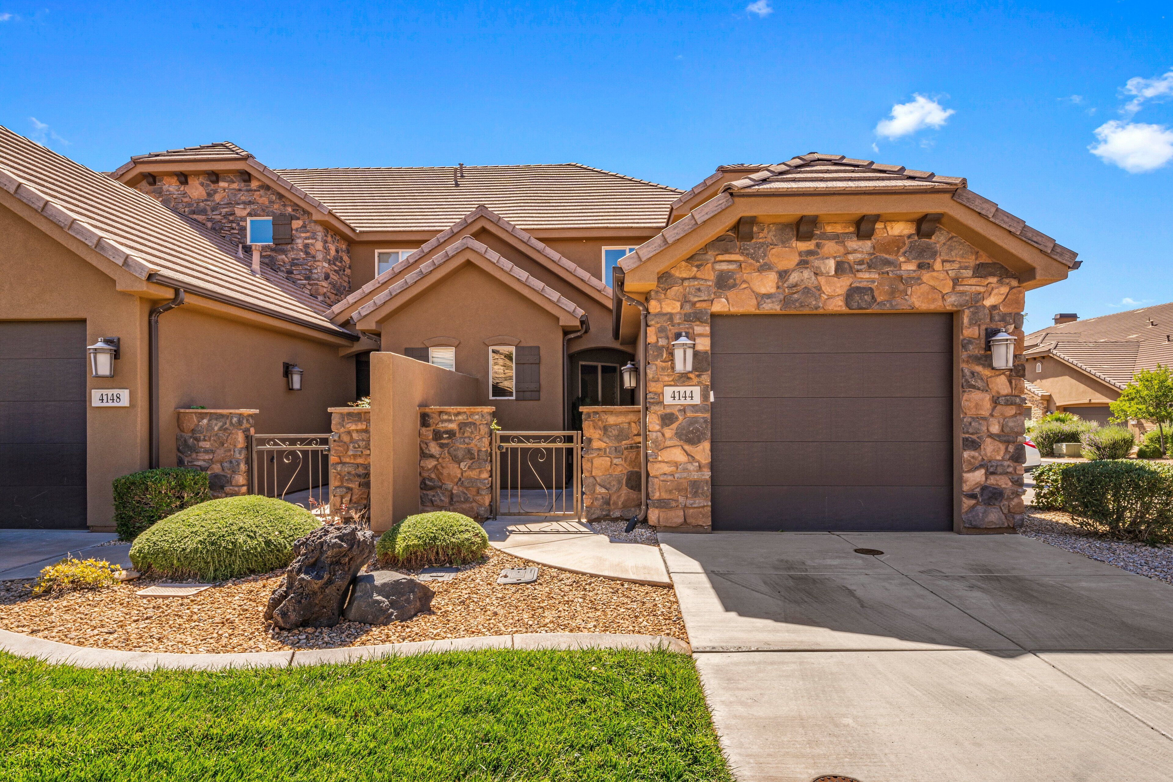 A two-story house with a stone facade, a garage, and a well-maintained front yard with a rock feature and trimmed bushes.