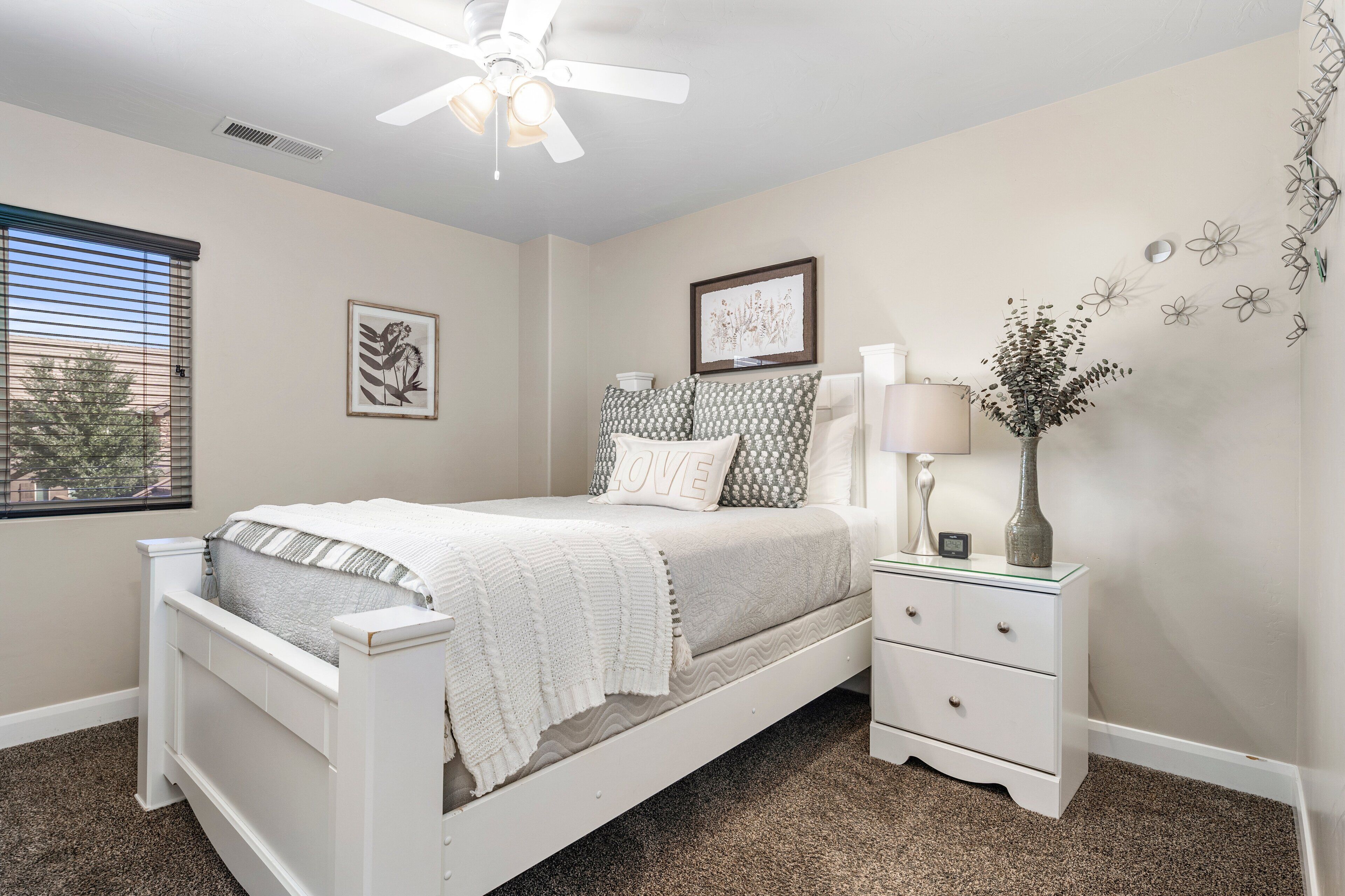 Un dormitorio con cama blanca, mesita de noche, lámpara y decoración en la pared.