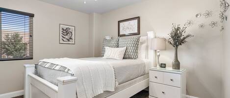Un dormitorio con cama blanca, mesita de noche, lámpara y decoración en la pared.