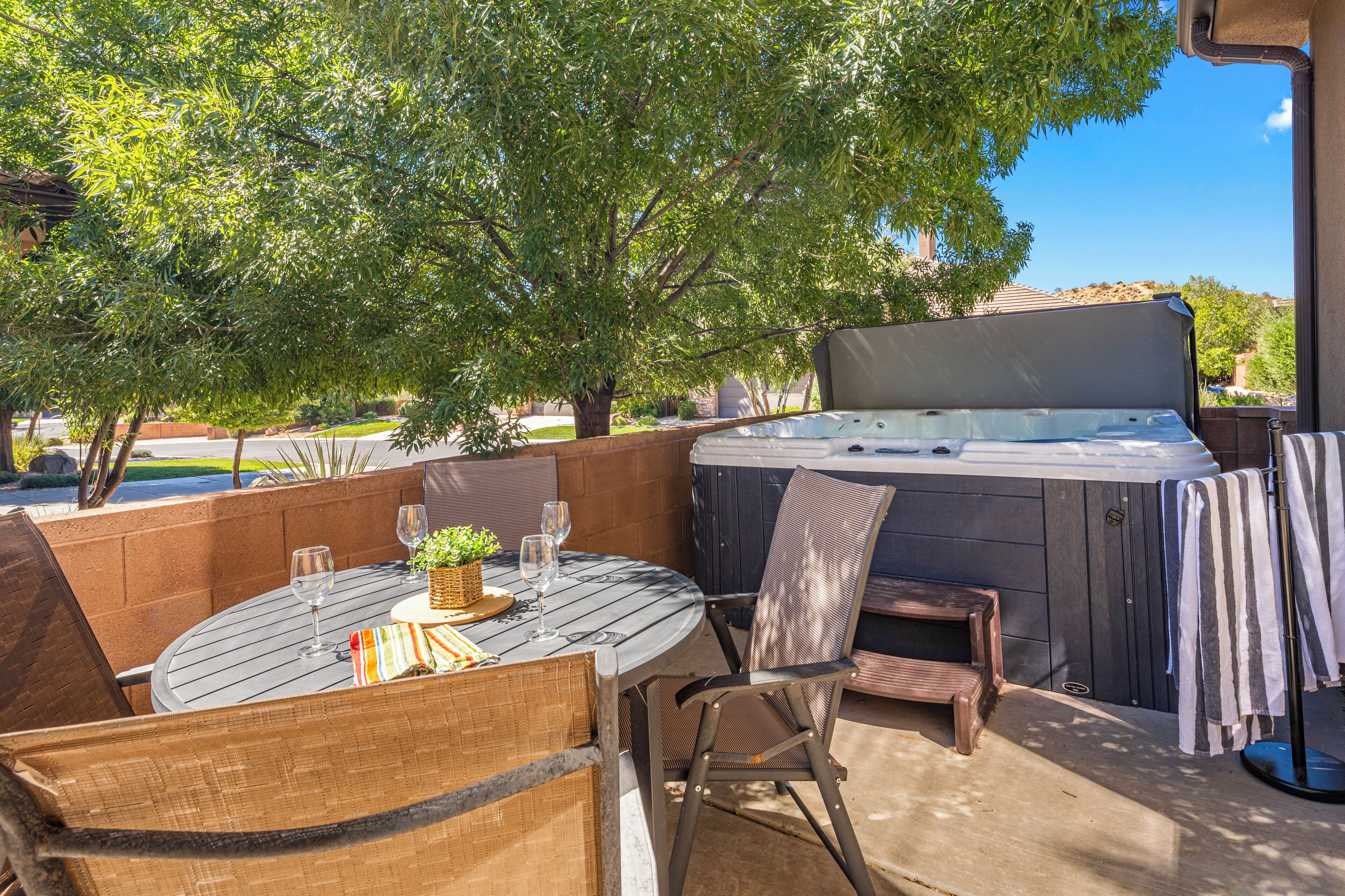 An outdoor patio with a round table, chairs, a hot tub, and a view of a residential area.