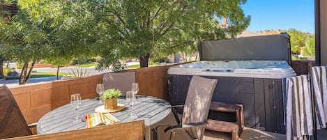 An outdoor patio with a round table, chairs, a hot tub, and a view of a residential area.