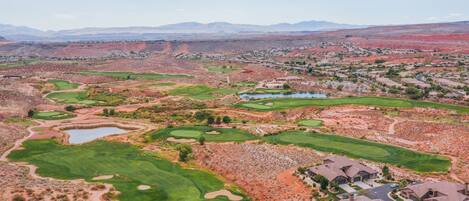 A golf course with multiple greens and bunkers, surrounded by residential areas and distant mountains.