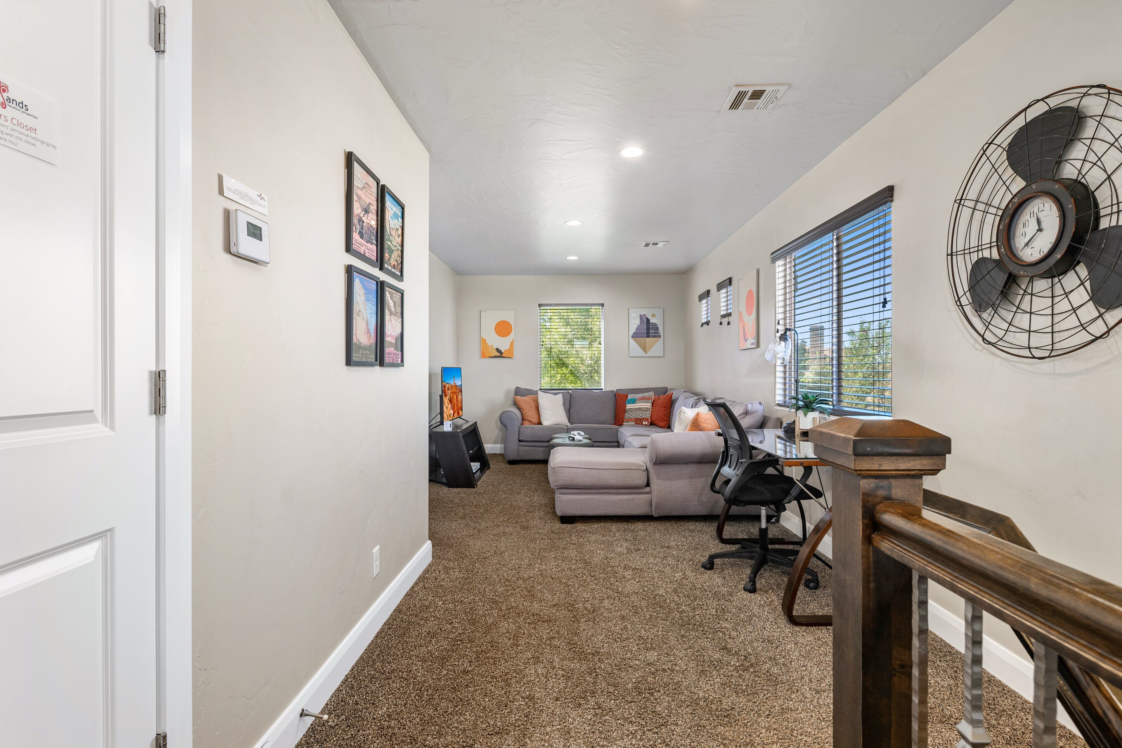 A living room with a grey sofa, a wooden desk, and a large fan on the wall.