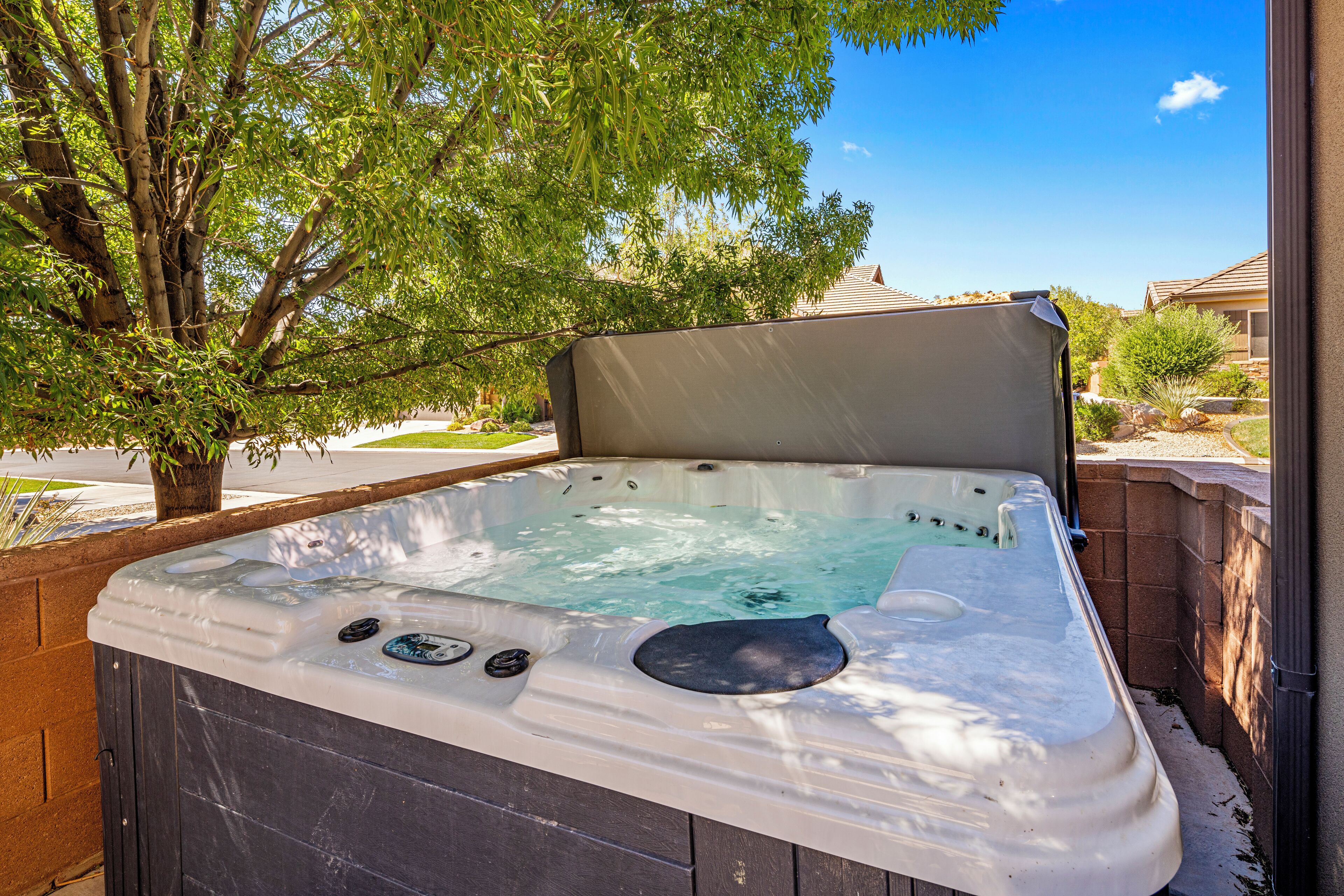 A hot tub with a cover, surrounded by a brick wall and a tree.