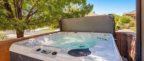 A hot tub with a cover, surrounded by a brick wall and a tree.