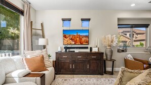 A living room with a large flat-screen TV mounted on the wall, a dark wooden cabinet, a beige sofa, and a patterned rug. - Coral Ridge 4144, Hot Tub, Bikes, Scooters, and near Coral Canyon Golf Course, SLP 12 (Washington)