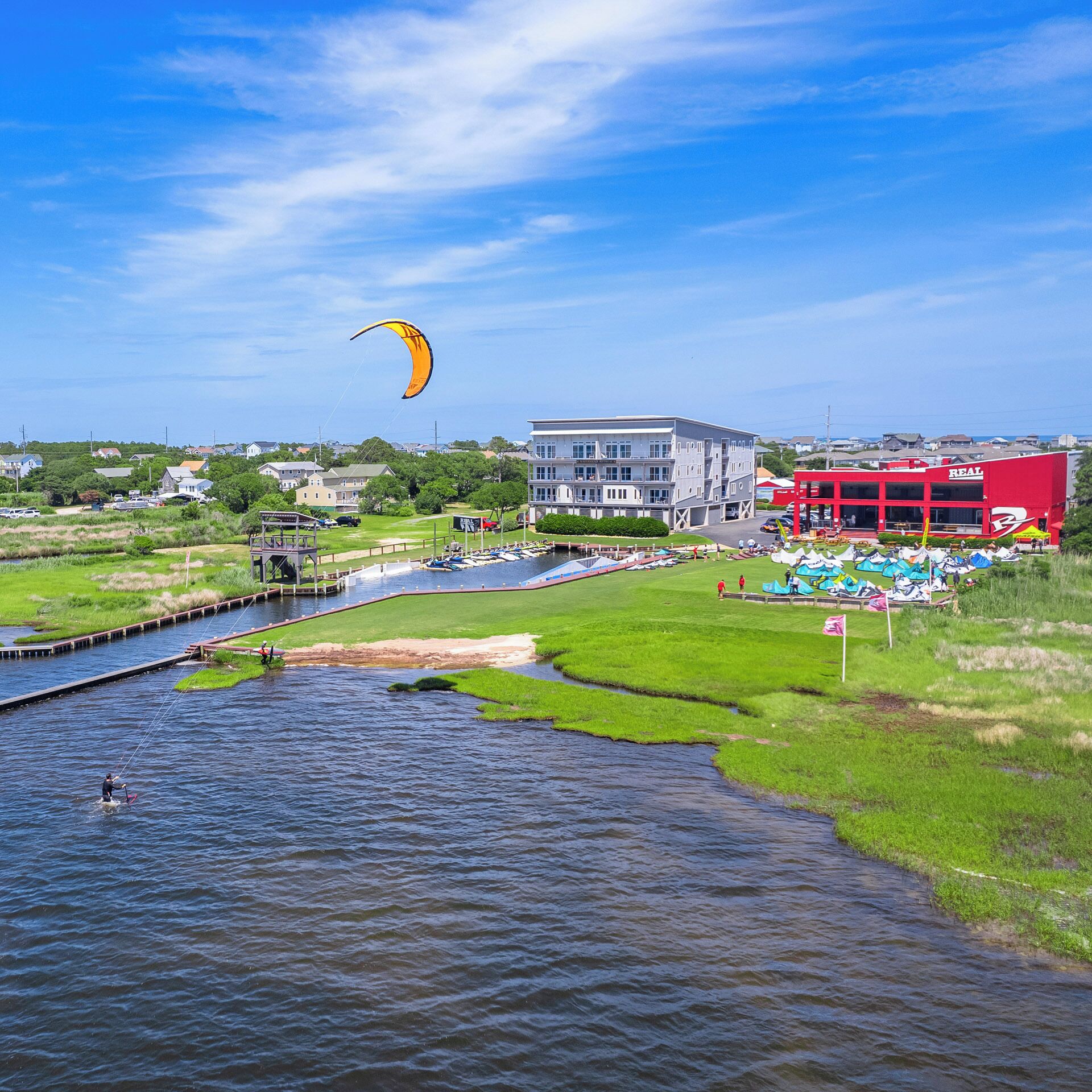A riverside view with a parasail, a marina, and buildings including a red 'REAL' sign.