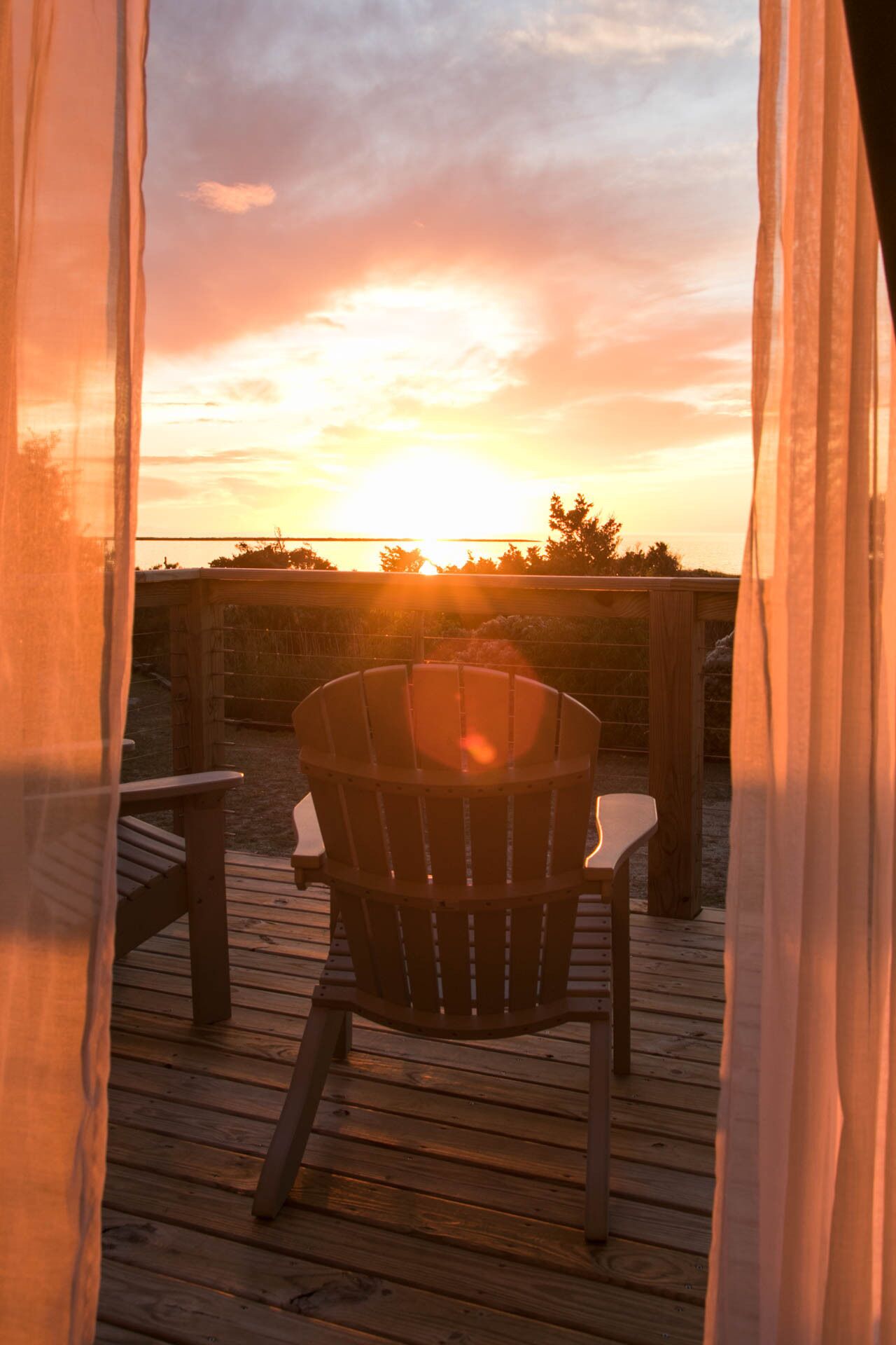 A wooden deck with a wooden chair facing a sunset.