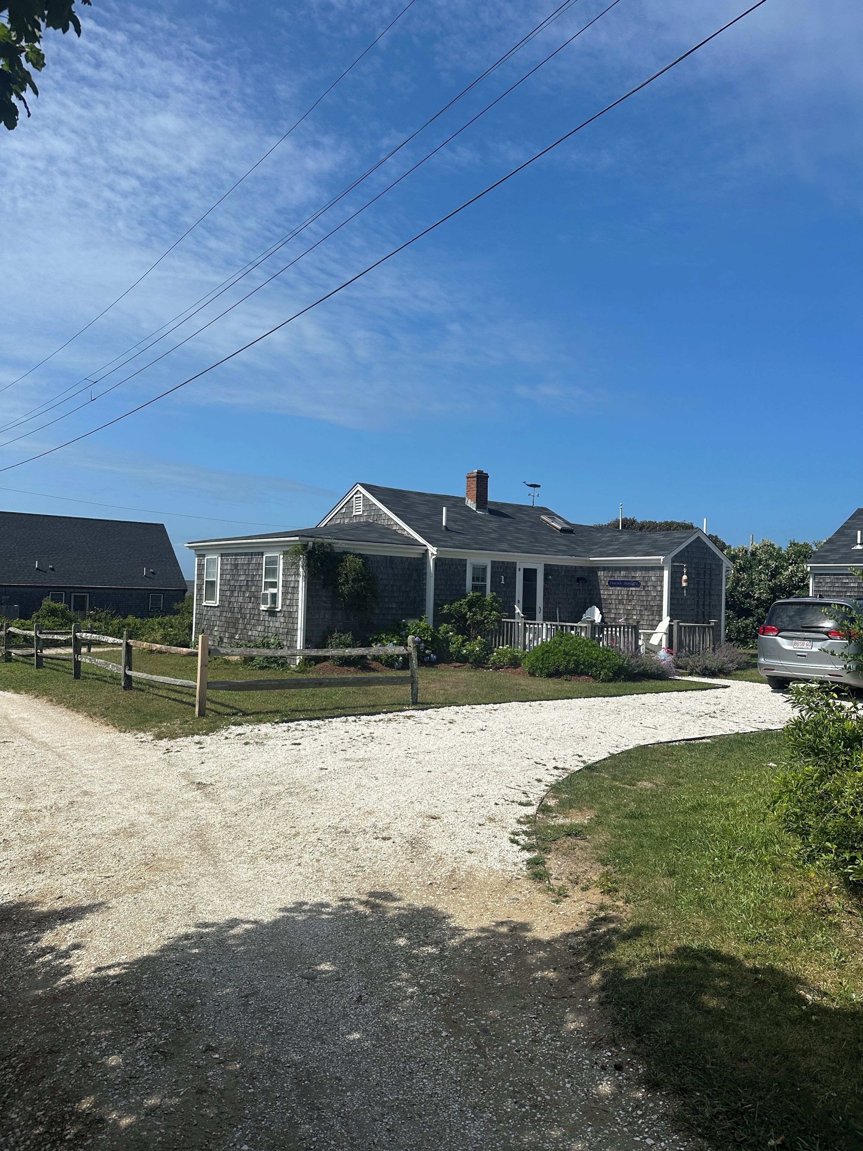 A two-story house with a gravel driveway, a fenced yard, and a clear blue sky.