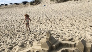 A sandy beach with a large sandcastle and a child playing nearby.