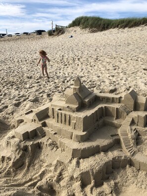 A sandy beach with a large sandcastle and a child playing nearby. - Frankie Starlight  - Classic Madaket Beach Cottage • Water Views • Sleeps 10 (Nantucket)