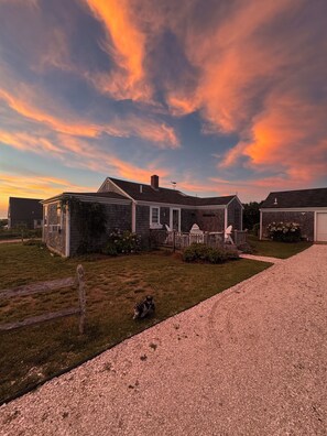 A residential property with a paved driveway, a grassy lawn, and a wooden fence.