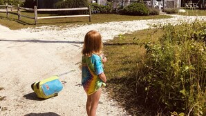 A child standing on a gravel path with a beach house in the background.