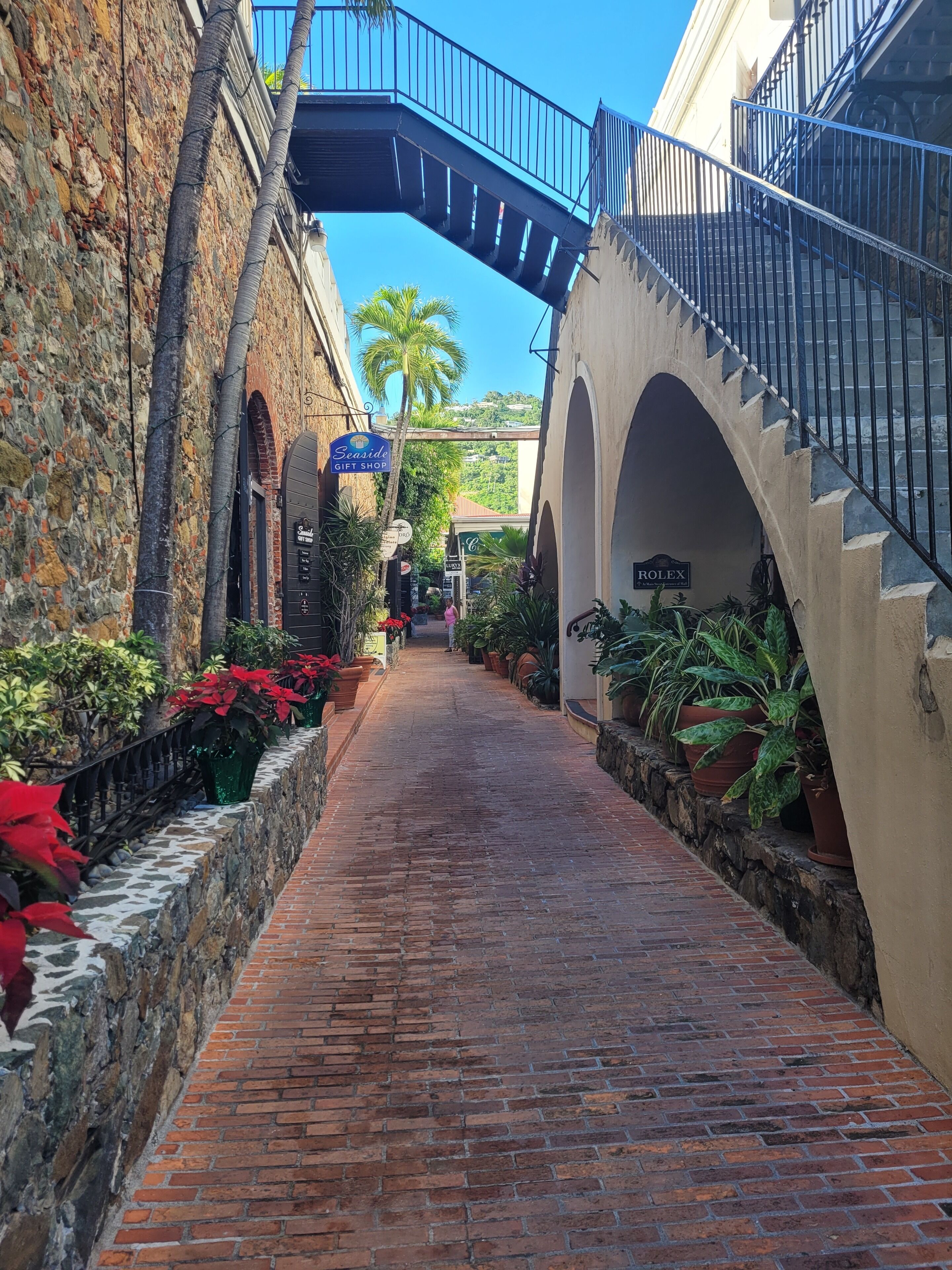 A brick pathway flanked by stone walls and potted plants, leading to a building with a sign for 'Seaside Gift Shop'.