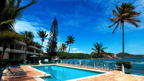 A pool area with lounge chairs and palm trees, overlooking the ocean. - REMODELED 2026! Prime OCEANFRONT POOLSIDE 2BR/2BA Condo-BEST location+Generator (St Thomas)