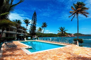 A pool area with lounge chairs and palm trees, overlooking the ocean. - REMODELED 2026! Prime OCEANFRONT POOLSIDE 2BR/2BA Condo-BEST location+Generator (St Thomas)