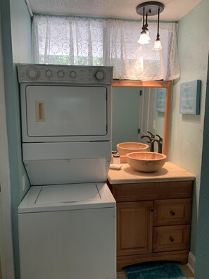 Una cocina compacta con estufa blanca, pileta de dos bañeras, alacenas de madera y un espejo.
