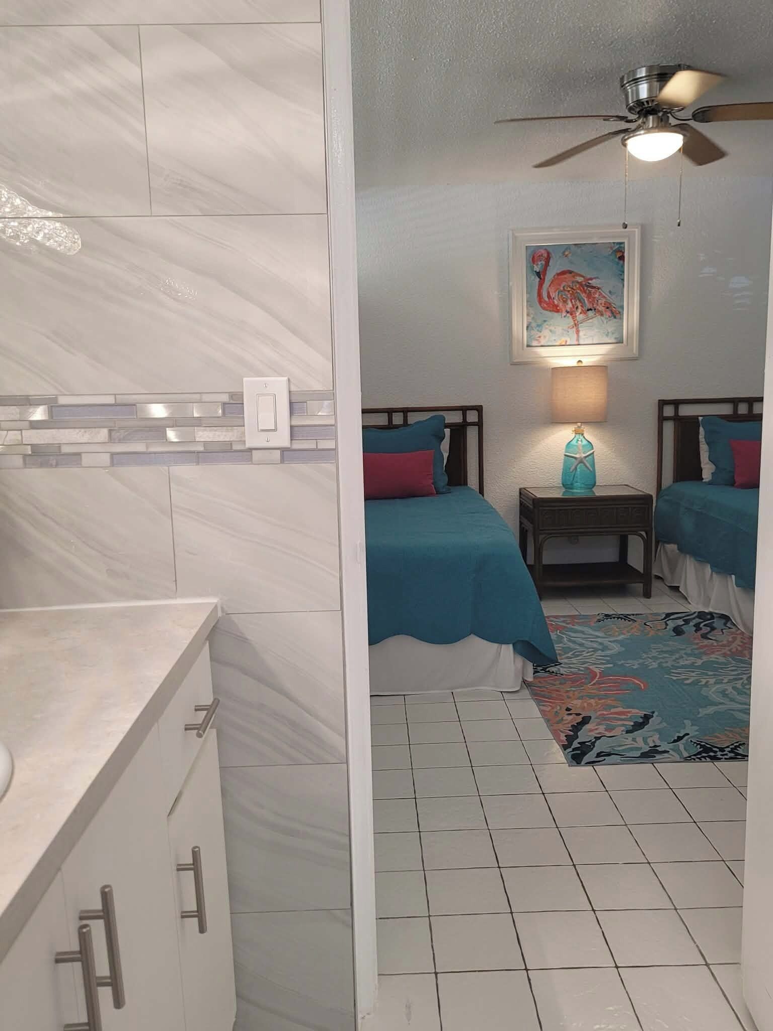 A hotel room with a bed, a nightstand, a ceiling fan, and a painting on the wall.