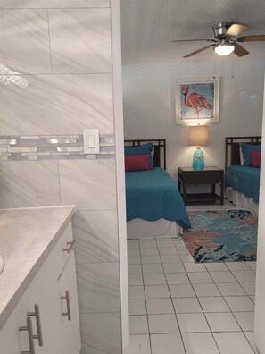 Een hotelkamer met een bed, nachtkastje, plafondventilator en een schilderij aan de muur.