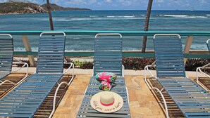 A row of blue lounge chairs with a hat and a colorful bag on the table. - REMODELED 2026! Prime OCEANFRONT POOLSIDE 2BR/2BA Condo-BEST location+Generator (St Thomas)